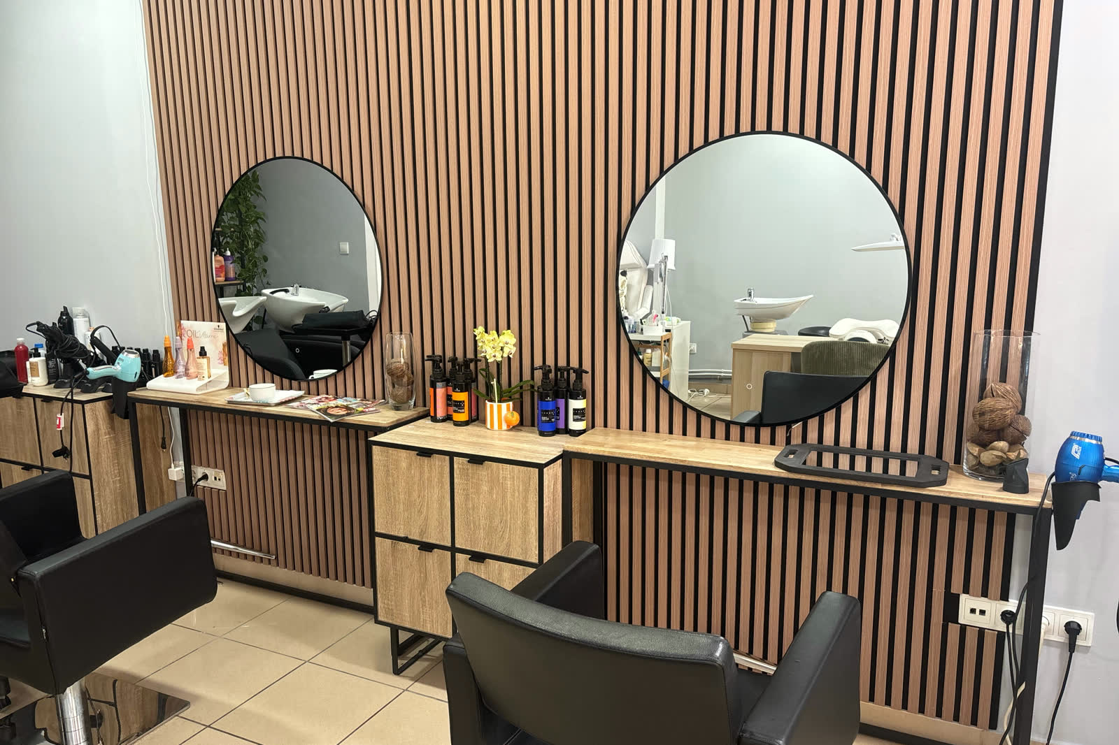 Zona de peluquería del salón, con dos espejos redondos sobre una pared de listones de madera